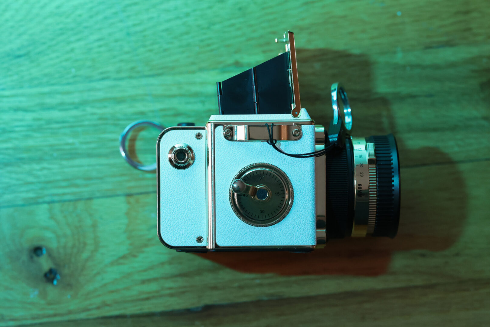 A toy camera under a green light against a wooden floor.
