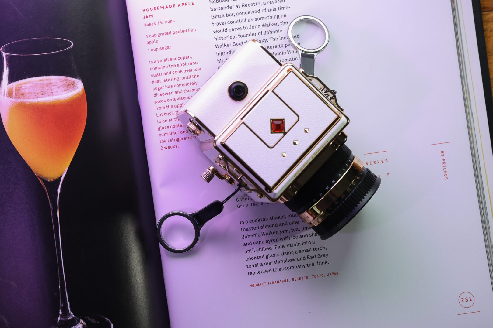 A toy camera on a book. There is a photo of a drink next to it. 