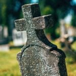 Old concrete christian cross tombstone on a cemetery graveyard burial ground, selective focus