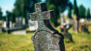 Old concrete christian cross tombstone on a cemetery graveyard burial ground, selective focus