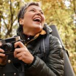 Senior woman laughs heartily as she captures memories with her camera on a forest hike.
