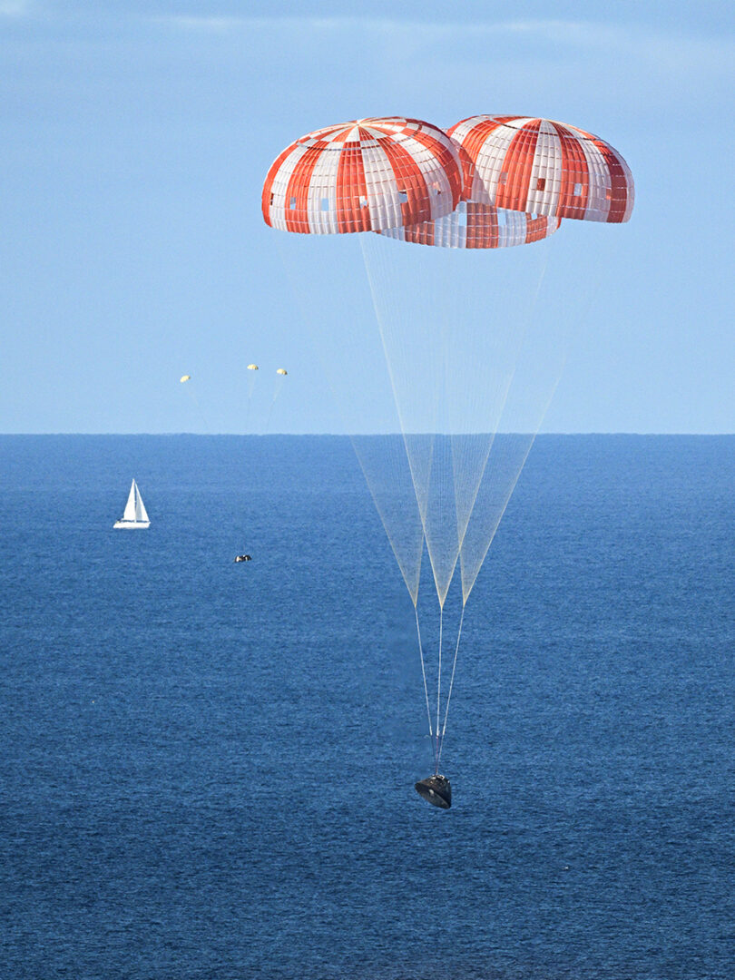 NASA’s Orion capsule descends under its main parachutes over the Pacific Ocean following a successful 10-day Artemis II mission, April 10, 2026. Credit: Josh Valcarcel