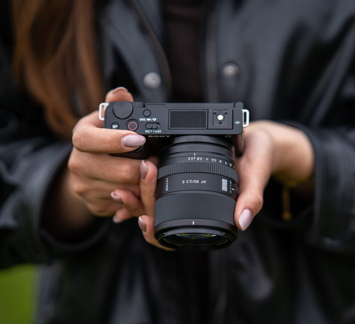 A woman holding a Sony camera with the Viltrox 90mm F2.2 EVO mounted on the camera.