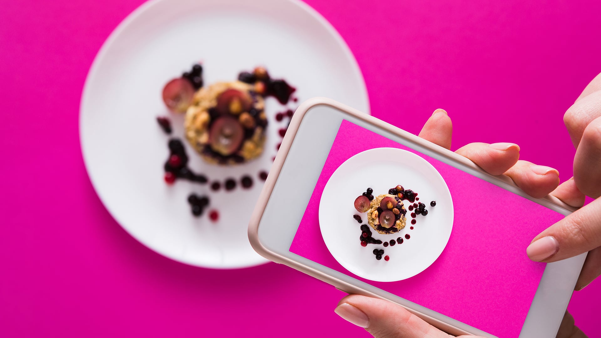 Top view close-up of female hands making flat lay food photo with phone for restaurant menu or social network. Oatmeal porridge on pink background, mockup, template, copy space, shallow depth of field