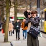 A man taking a photo with a grey Manfrotto UNCOVER Messenger Bag on his shoulder.