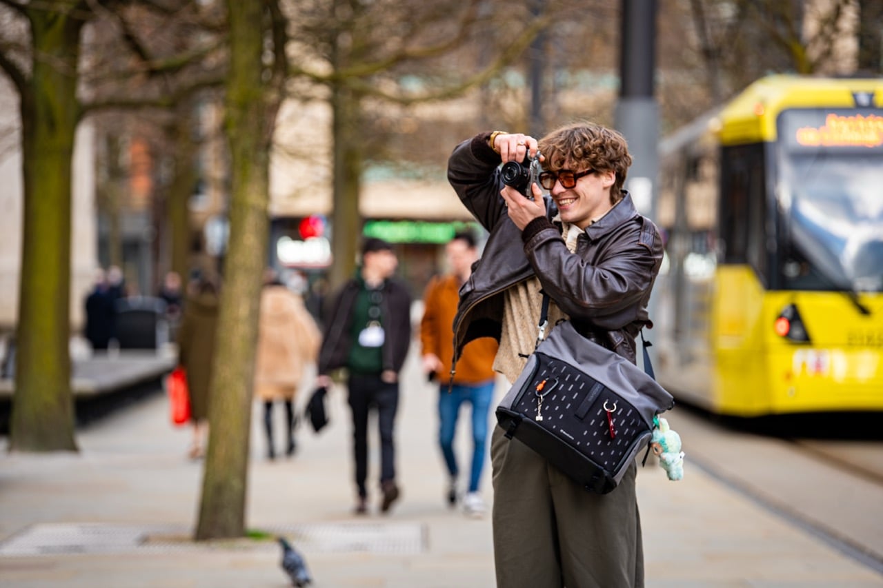 A man taking a photo with a grey Manfrotto UNCOVER Messenger Bag on his shoulder.