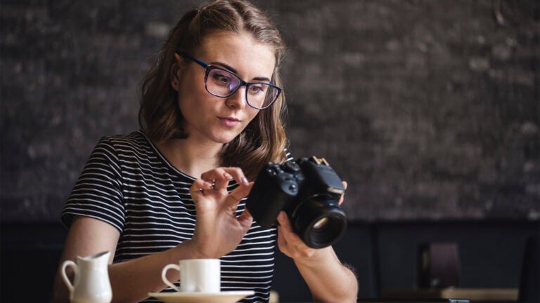 Young woman photographing chimping her latest photos on the rear screen of her camera as she sits relaxing having coffee at a restaurant