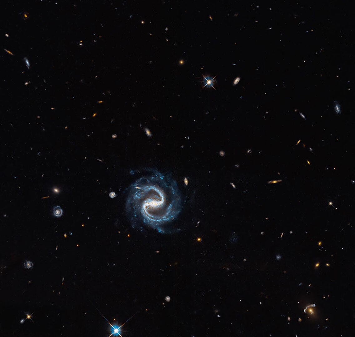 A spiral galaxy (center) appears in the same field of view as a vivid gravitational lens (right corner) in this Hubble image. Credit: NASA, ESA, and X. Huang (University of San Francisco)